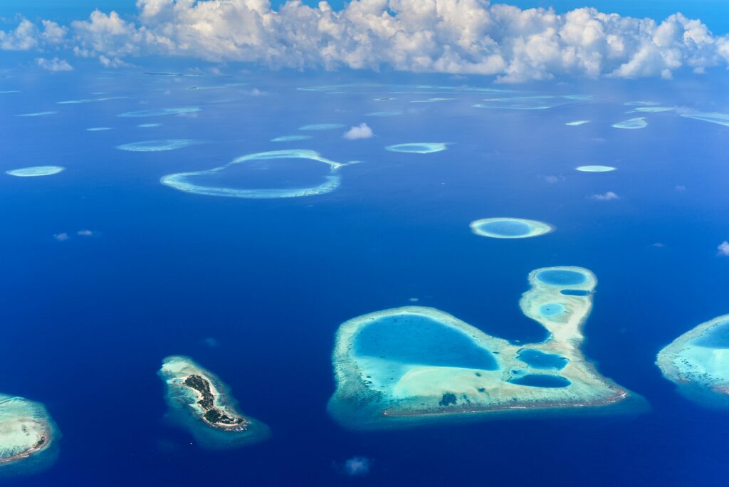 Breathtaking aerial view of turquoise atolls surrounded by deep blue ocean under a vibrant sky.