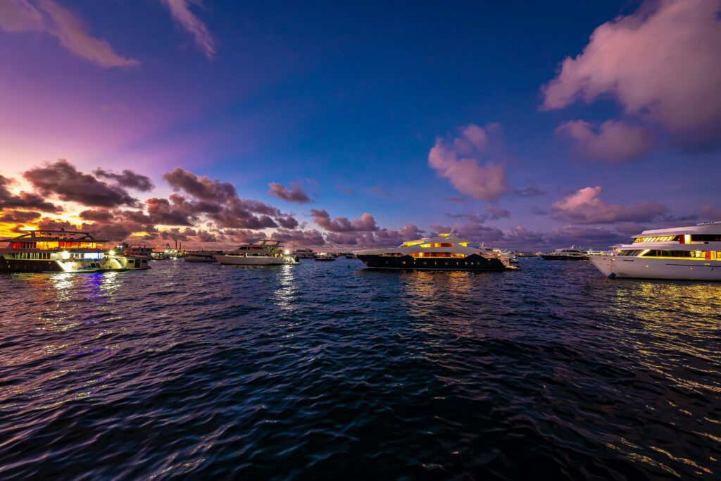 A serene sunset view of luxury yachts anchored in the Maldives, reflecting vibrant colors on the water.