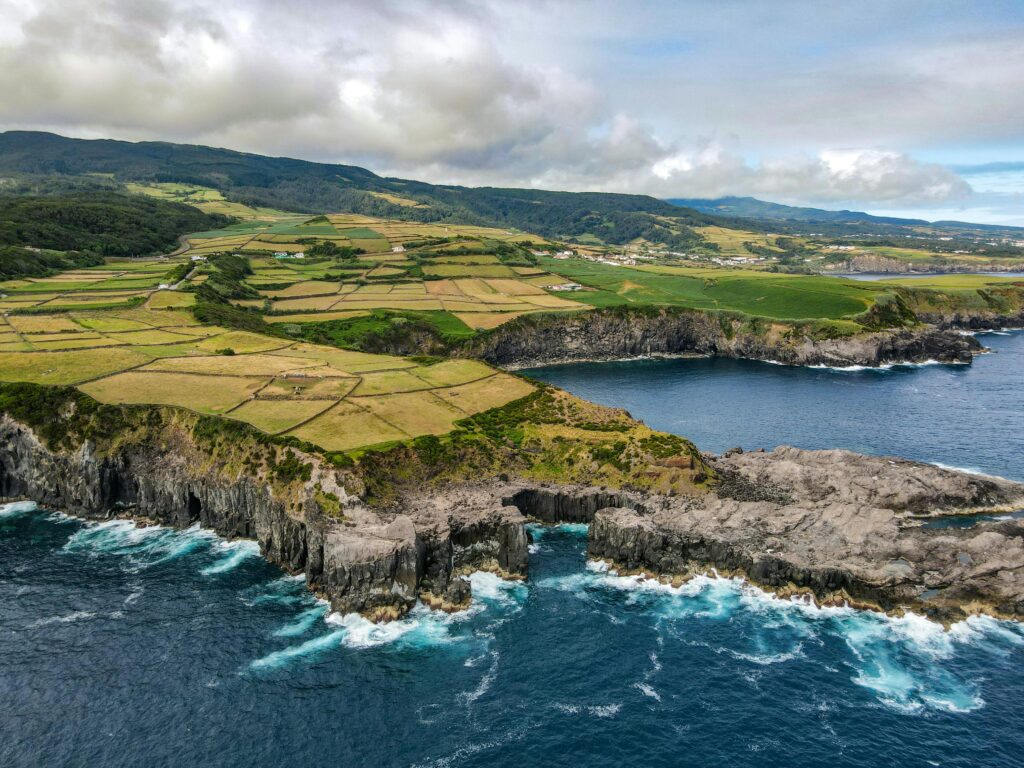 A breathtaking aerial view of coastal cliffs and lush farmlands under a cloudy sky.
